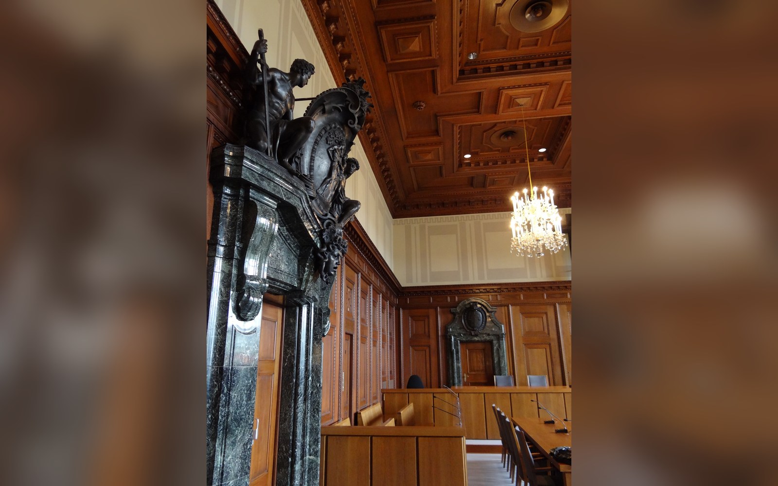 A carved marble figure tops the doorway of a wood-paneled courtroom with a crystal chandelier